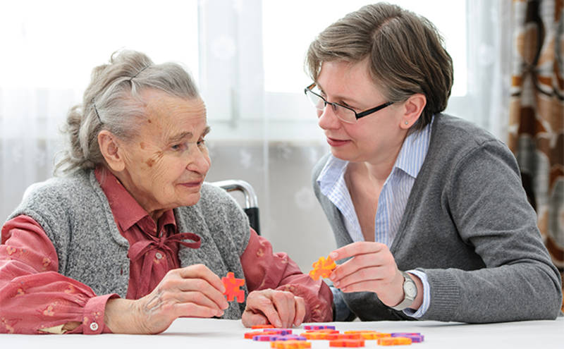 Ältere Dame mit ihrer Betreuerin beim Puzzeln