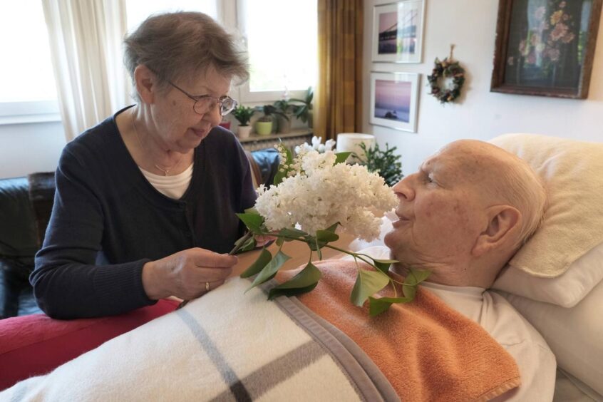 Ältere Dame mit frischen Blumen am Bett eines Senioren
